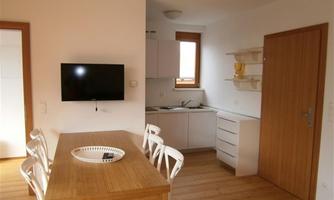 Modern kitchen with a dining area and a TV. Bright walls and wooden floor create an inviting atmosphere.