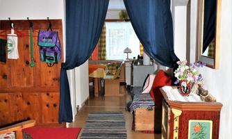 A cozy hallway with wooden panels and colorful rugs. On the left side, there are comfortable furniture and decorative elements.