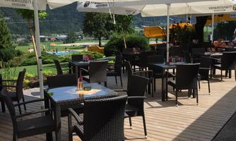 An inviting terrace with black garden furniture and umbrellas. In the background, a green meadow can be seen.