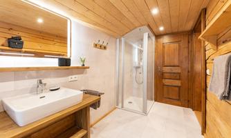 A modern bathroom with wooden paneling and a sink. There is a shower and a wooden cabinet door, which give the room a cozy atmosphere.