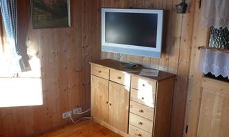 A cozy room with wooden walls and a television on a wooden dresser. A window lets in natural light and creates a warm atmosphere.