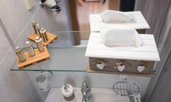 A modern bathroom with a decorative tissue box and care products on a shelf. The room is bright and invitingly designed.