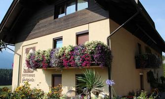 A guesthouse with colorful flowers on the balconies. The sky is clear and the surroundings are green and picturesque.