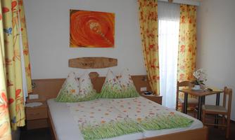 A bright room with a double bed and colorful curtains. There is a small table and a beautiful wall decoration.