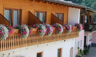 A beautiful balcony with blooming plants and colorful flower boxes. The upper part of the house has wooden cladding and large windows.