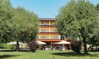 A beautiful hotel building surrounded by green grass and trees. On the terrace, there are sun umbrellas and tables, perfect for relaxed moments outdoors.