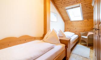 A cozy bedroom with two single beds and wooden paneling. A small armchair and a skylight give the room an inviting atmosphere.