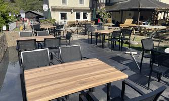 A cozy outdoor area with wooden chairs and tables. In the background, a building and a green environment can be seen.