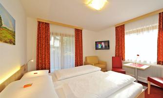 A cozy hotel room with two beds and a modern television. Large windows provide plenty of daylight and an inviting atmosphere.