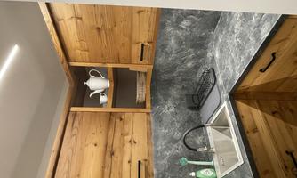 A modern kitchen with wooden furniture and a gray countertop. Dishes and kitchen utensils are on the shelf.