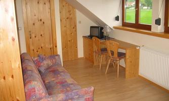 A cozy room with a colorful sofa and a desk. Large windows let in plenty of light and offer a view of the greenery.