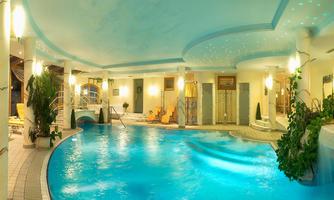 An elegant indoor pool with blue water and gentle lighting. Surrounded by plants and comfortable loungers, the area radiates calm and relaxation.