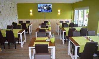 A modern restaurant with brown chairs and white tables. The walls are painted in a fresh green, and a television is mounted on the wall.