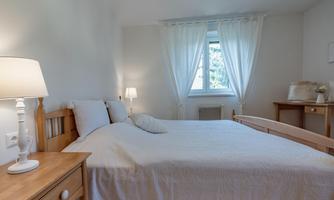 A bright bedroom with a double bed and a white duvet. Soft light through the windows and a cozy atmosphere.