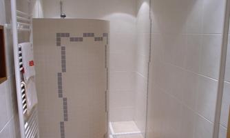 A modern shower with bright tiles and a neutral color scheme. The floor is decorated with an orange towel.