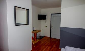 A simply furnished room with a mirror and a TV on the wall. The walls are painted in neutral colors, and a table with a chair is in the room.