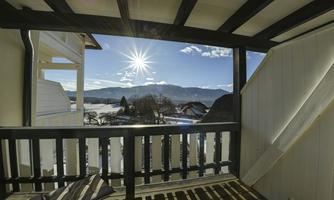A view from a balcony with a mountain landscape in the background. The sun is shining in the clear sky.