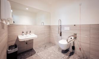 A modern bathroom with a sink, a toilet, and a mirror. The walls are bright and the floor is made of stone-like tiles.