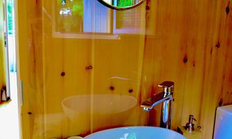 A modern bathroom with a round mirror and an elegant sink. The walls are made of light wood, creating a warm atmosphere.