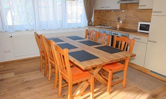 An inviting dining area with a large wooden table and orange chairs. The kitchen is modern and well-equipped, with plenty of natural light.