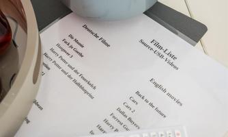 A bowl of peanuts is next to a remote control and a list of movie titles. The background is bright and modern designed.
