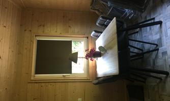 A cozy room with wooden walls and a large table in the middle. Around the table are chairs and a window with a privacy screen, letting light in.