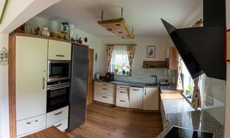 A modern kitchen with wooden flooring and light cabinets. It is well-equipped with appliances and has large windows for plenty of daylight.