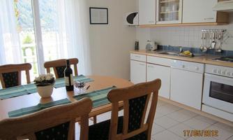A bright kitchen with a dining table and chairs. There is a wine and a flower vase on the table.