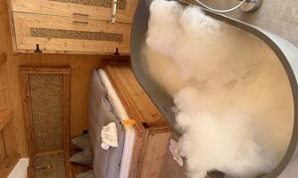 A cozy room with a wooden bed and a modern bathtub full of foam. The natural wood look creates a relaxed atmosphere.