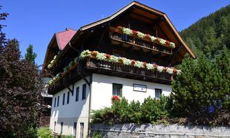 A traditional Alpine house with balconies full of flowers. The clear sky and the surrounding nature give the scene a peaceful atmosphere.