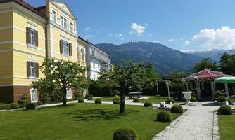 A beautiful garden with a well-maintained lawn and trees. In the background, an elegant building and the mountains are visible.