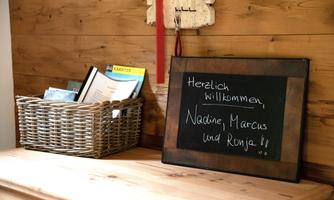 A welcome sign on a wooden surface that presents names. Next to it is a basket with brochures and booklets.