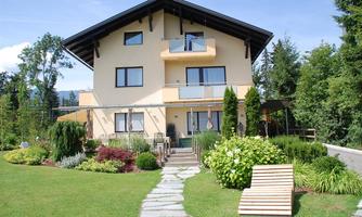 A modern house with a well-kept garden and a green surroundings. The path to the entrance is paved with cobblestones.
