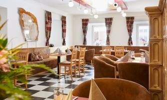 A cozy restaurant with elegant furnishings and a modern ambiance. The black-and-white tiled floor and the stylish curtains create an inviting atmosphere.