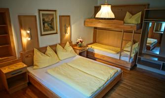 A cozy room with a double bed and a bunk bed. The wooden furniture and soft lighting create an inviting atmosphere.