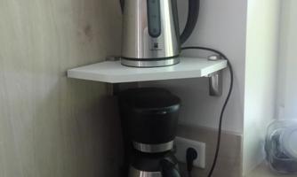 A kettle and a coffee maker are on a shelf in a modern kitchen. The appliances are made of stainless steel and are next to a wall.