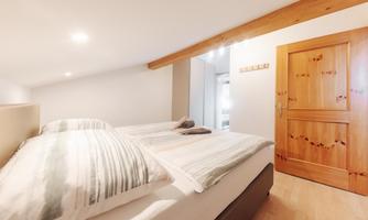 A cozy bedroom with two beds and bright wood decor. The walls are in neutral colors, and the room feels inviting and friendly.