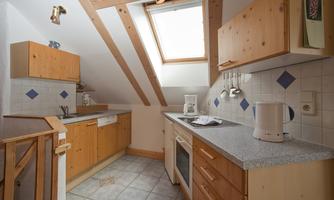 A cozy attic kitchen with wooden cabinets and bright tiles. A window provides daylight and an inviting atmosphere.