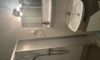 A modern bathroom with a shower stall and a sink. There is a mirror and a shelf on the wall.