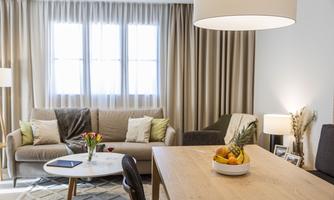 A modern living room with a cozy sofa and a dining table. On the table, there is a decorative fruit bowl.