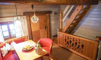 A cozy chalet with a wooden-paneled interior. There is a dining table with fresh fruit and a staircase leading to an upper area.