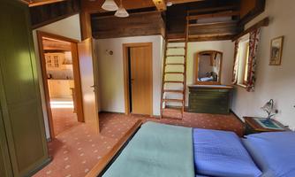 A cozy bedroom with two beds and wooden details. There is access to the kitchen and a ladder to an upper area.
