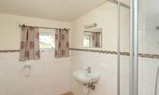 A modern bathroom with a shower, sink, and toilet. The walls are brightly tiled and there are windows with curtains.