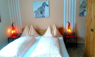 A comfortable bedroom with two beds and decorative pillows. There is also a wooden wardrobe and artistic lamps.