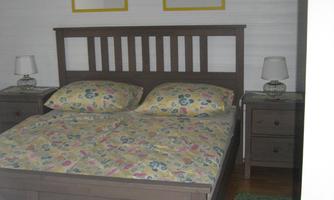 A cozy bedroom with a wooden bed and colorful bedding. On the walls hang two pictures, and beside the bed are nightstands with lamps.