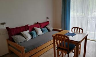 A cozy living space with a sofa bed and a wooden table. Large windows ensure plenty of daylight.