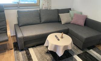 A modern furnished living room with a gray couch and a small table. Colorful cushions are on the couch, and the floor is covered with a carpet.