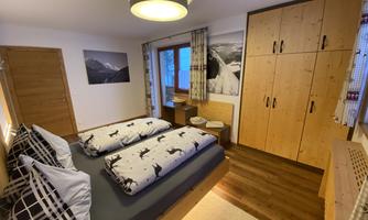 A cozy bedroom with two beds and a large wardrobe. The walls are decorated with natural wood paneling, providing a rustic atmosphere.
