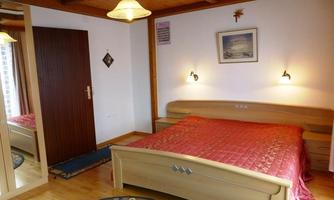 A cozy bedroom with a large bed and red bedding. The walls are light and the furniture is made of wood, with warm lighting.