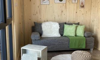 A cozy room with a gray sofa and colorful cushions. On the floor, there's a round rug and two small tables.